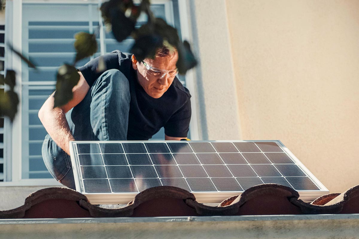 Person befestigt ein Solarmodul auf einem Dach.