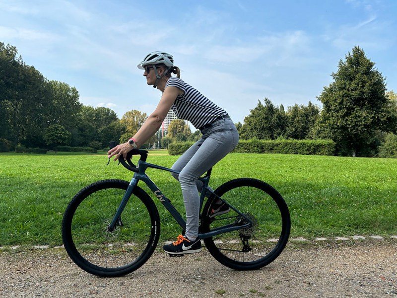 Frau fährt auf einem Gravcelbike durch eine Parklandschaft.