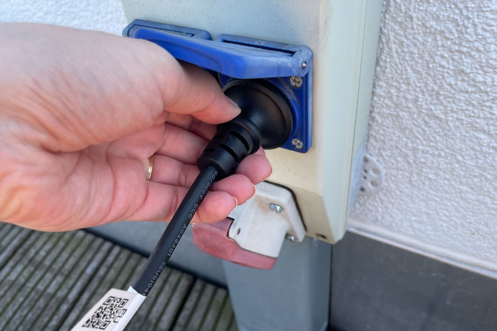 Eine Person steckt einen Schuko-Stecker in eine Außensteckdose.