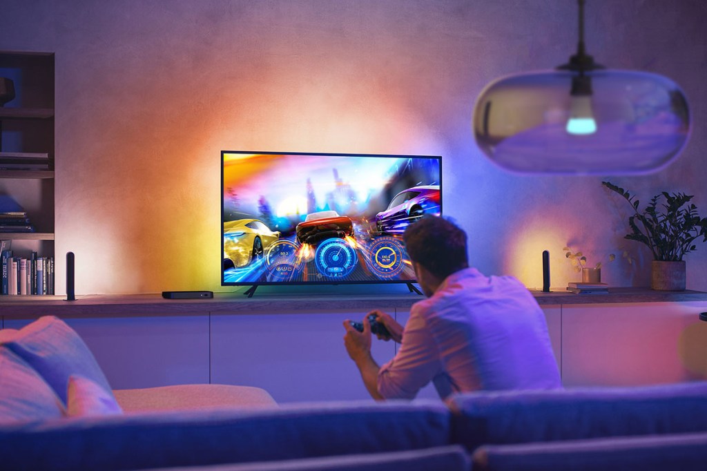 Mann sitzt auf Sofa vor beleuchteten Flachbild-TV mit Spielcontroller in den Händen.