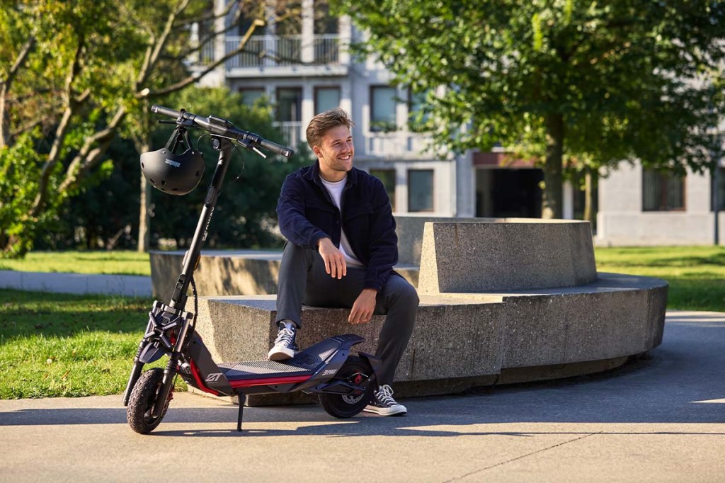 Mann sitzt auf einer Betonbank, vor ihm steht sein E-Scooter