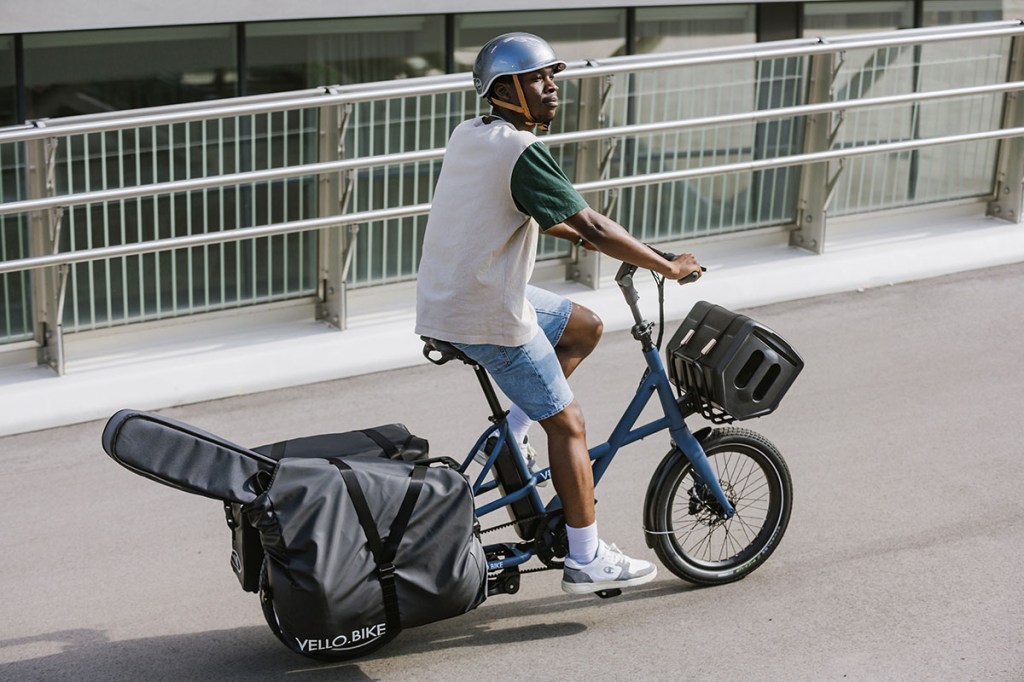 Mann fährt auf kompakten Vello Sub E-Cargo-Bike über eine Brücke. Dabei ist der Gepäckträger des Lastenrads mit Satteltaschen voll beladen.