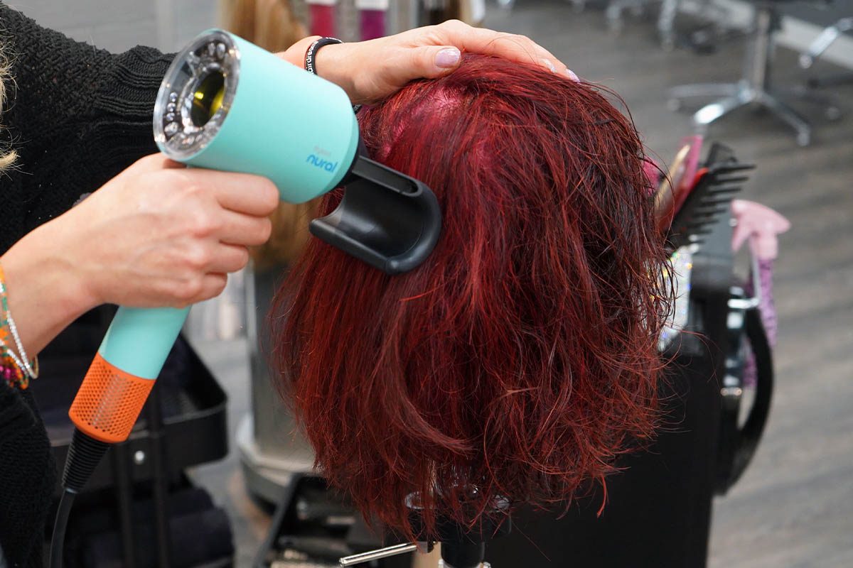 Eine Person föhnt einen lebensgroßen Puppenkopf mit dem Dyson Supersonic Nural und Aufsatz gegen Frizz.