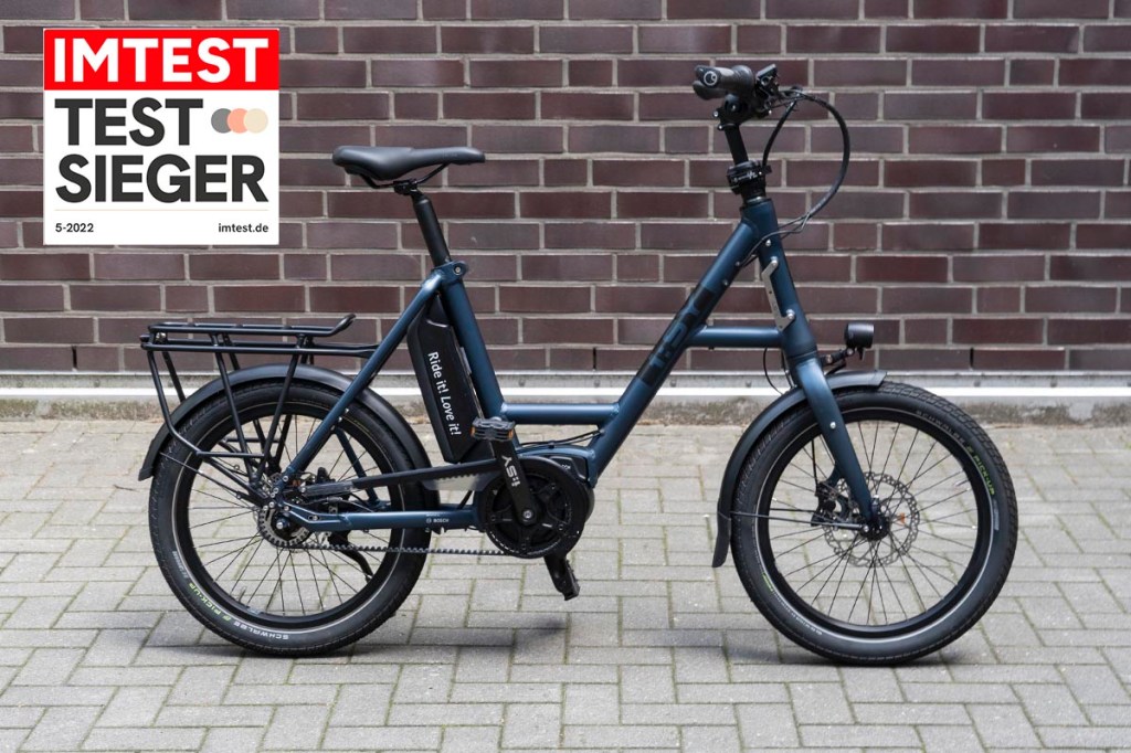 Kompakt E-Bike im Profil vor einer Mauer mit eingklinktem Testsieger-Siegel von IMTEST.