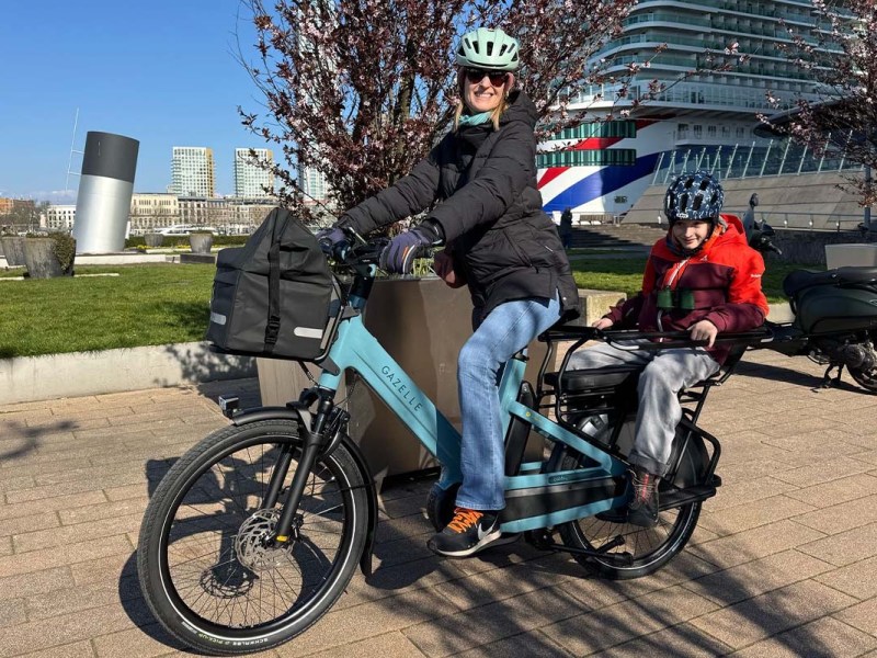 Frau auf einem Cargo-E-Bike, Kind sitzt hinten auf dem Rücksitz