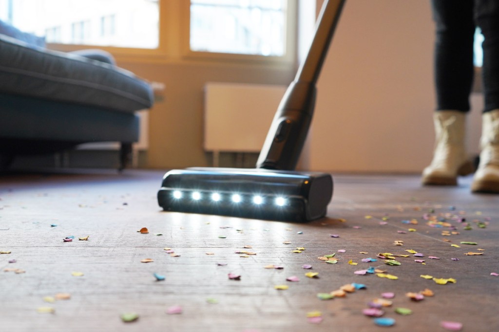 Eine Person saugt mit dem Bosch Unlimited 10 Konfetti von einem Holzfußboden. Die Düse hat mehrere weiße Lichter an der Vorderseite.