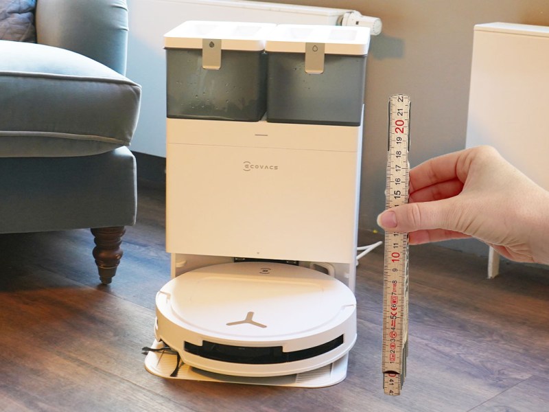 Der Ecovacs Deebot T50 Omni in seiner Station. Daneben hält eine Hand einen Zollstock.