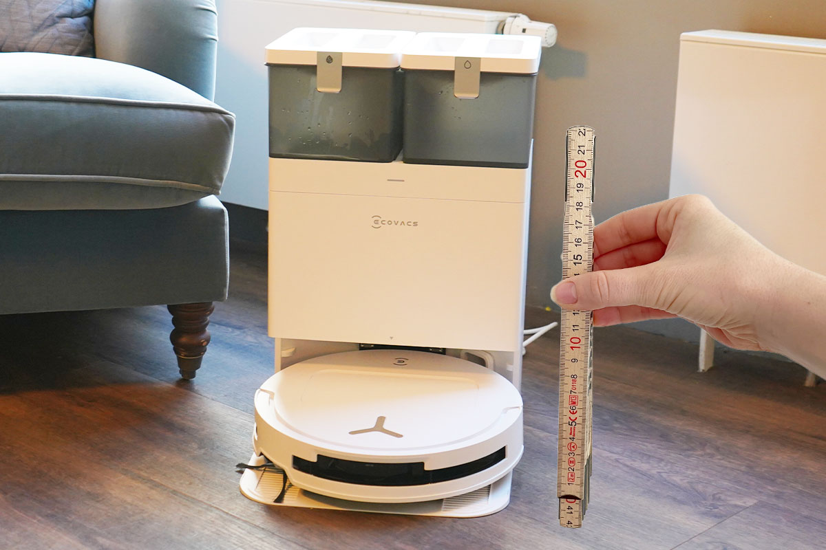 Der Ecovacs Deebot T50 Omni in seiner Station. Daneben hält eine Hand einen Zollstock.