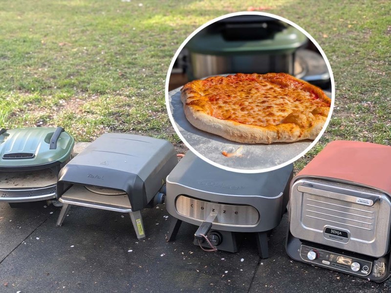 Vier Pizzaöfen nebeneinander auf Steinplatten stehend, ein rundes Fenster im Bild zeigt eine fertige Pizza