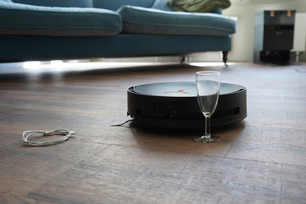 Der Saugroboter Deebot X8 Pro auf einem Holzboden schiebt ein Sektglas vor sich her.