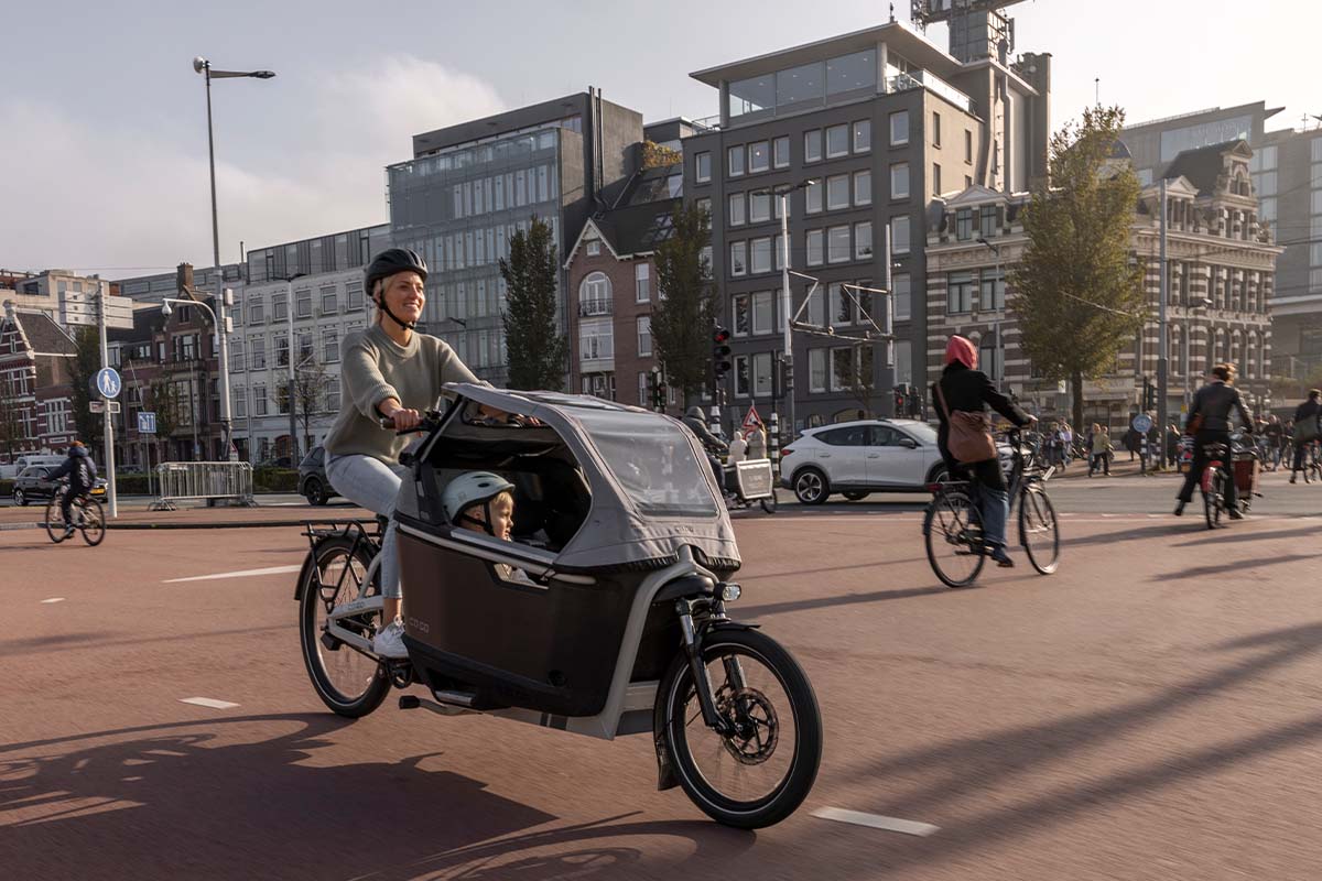 Frau fährt mit einem Cargo-E-Bike, in dem Kinder sitzen, durch eine belebte Stadt