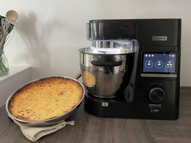 Der eingeschaltete Kenwood Cooking Chef in der Sallys Edition auf einer Küchenarbeitsplatte. Daneben steht eine Quiche.