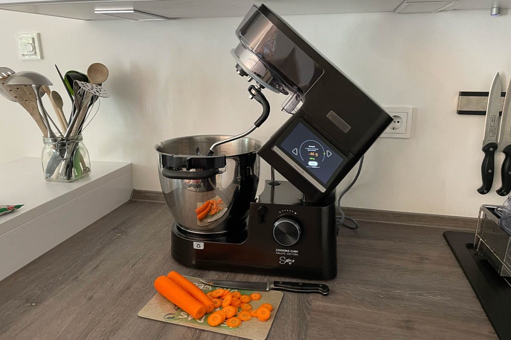Der Kenwood Cooking Chef Sallys Edition auf einer Arbeitsplatte. Davor ein Brettchen mit Möhren und Messer.