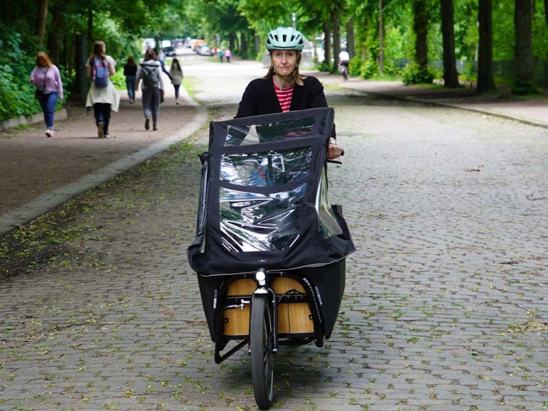 Frau fährt mit einem Cargo-E-Bike eine straße lang, fährt auf die Kamera zu