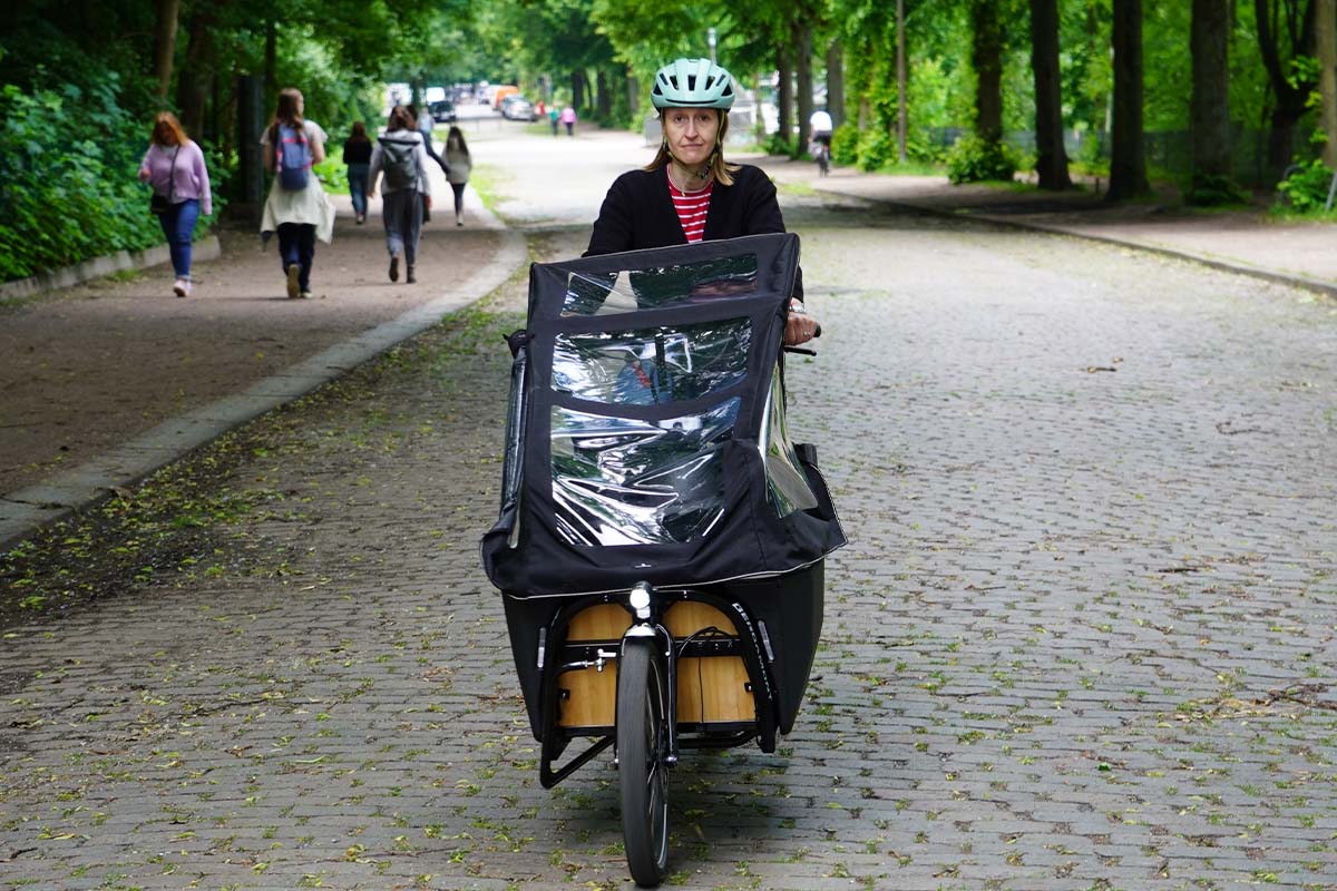Frau fährt mit einem Cargo-E-Bike eine straße lang, fährt auf die Kamera zu