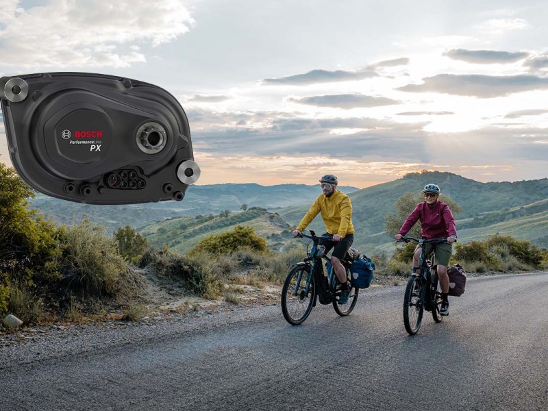 zwei Radfahrer fahren über eine einsame Straße inmitten der Natur, im Bild zudem zu sehen: eine großaufnahme des neuen Bosch-Motors