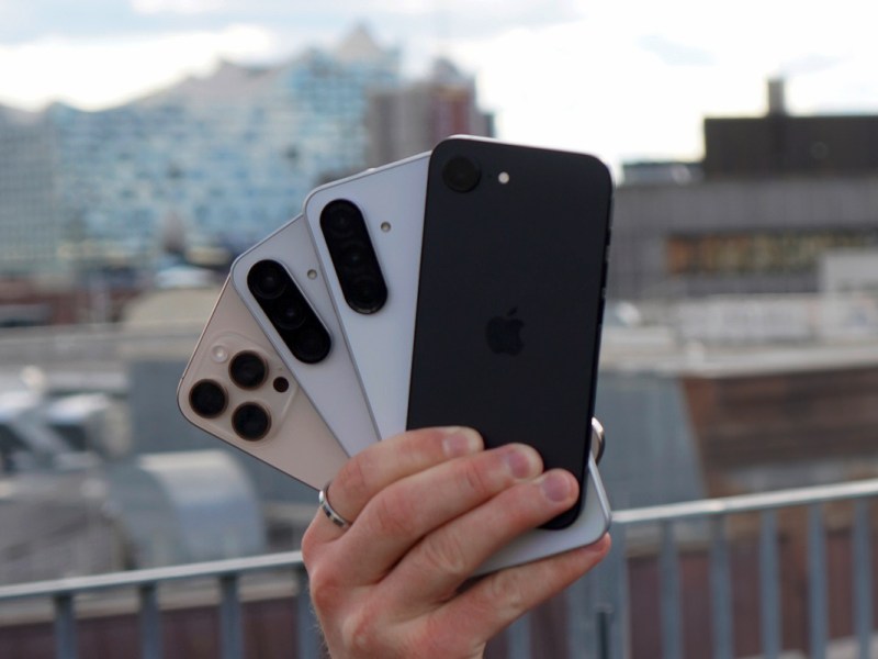 Eine Hand hält vier Smartphones hoch.