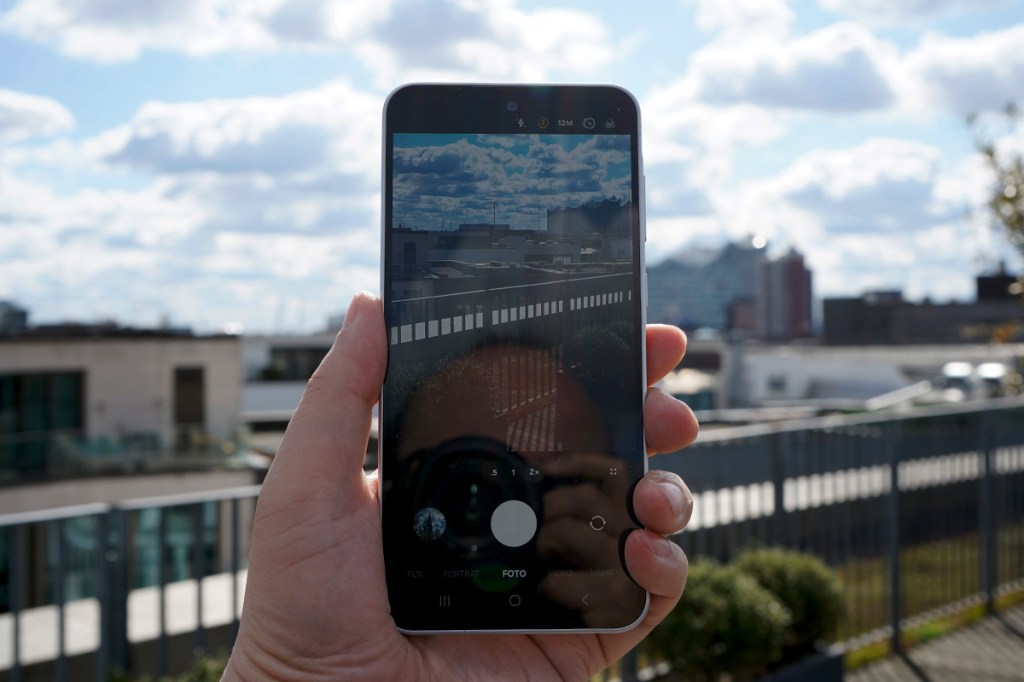 Eine Hand hält ein Smartphone hoch, auf dem Bildschirm ist die Kamera-App zu sehen.