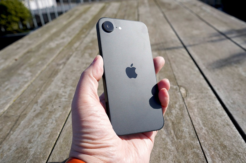 Eine Hand hält das iPhone 16e mit der Rückseite nach vorne.