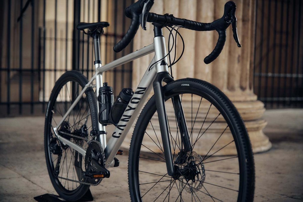 silbernes Gravelbike schräg von vorne vor einer Säule stehend