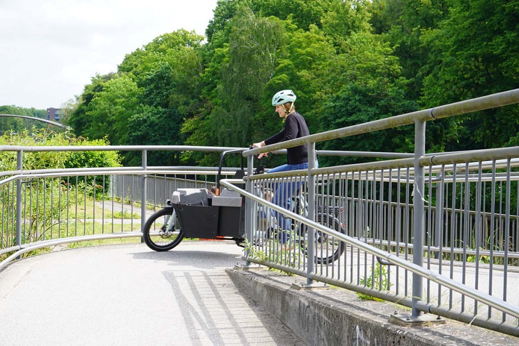 Frau fährt mit einem Cargo-E-Bike eine enge Kurve 