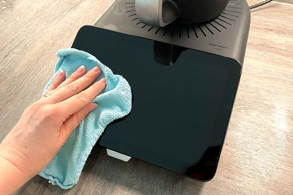 Eine Hand wischt das Display des TM7 mit einem blauen Tuch ab.