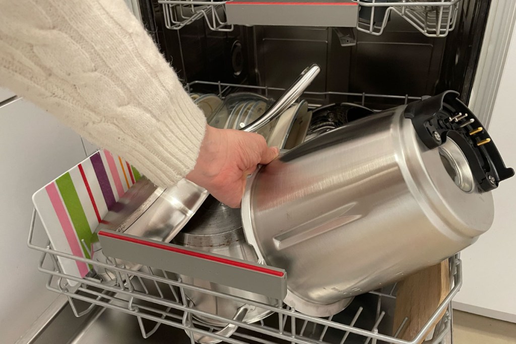 Eine Person gibt den Edelstahlteil des TM7-Mixtopfes in eine gefüllte Spülmaschine.